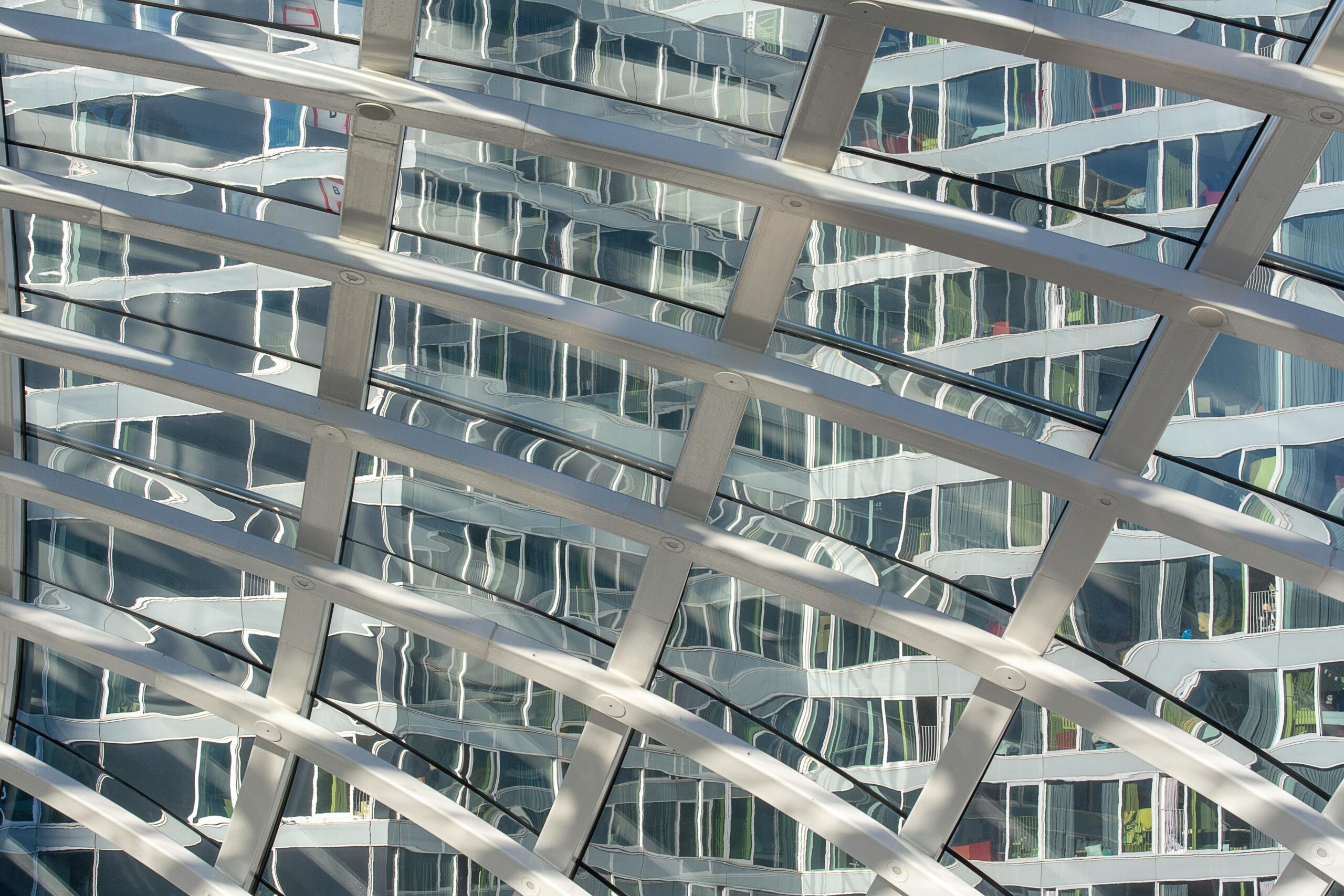 Curvilinear glass facade reflects surrounding buildings in a modern urban setting.